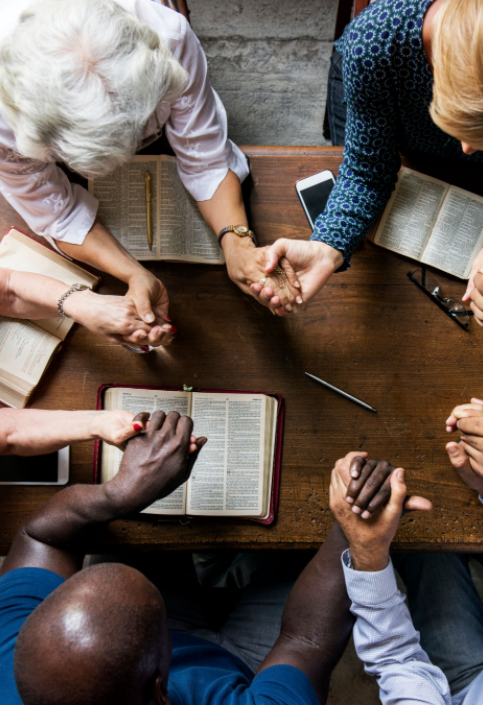 group of people holding hands with bibles on a table